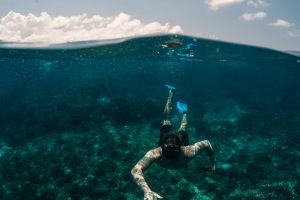 A vertical shot of male swimming underwater with the sky in the background